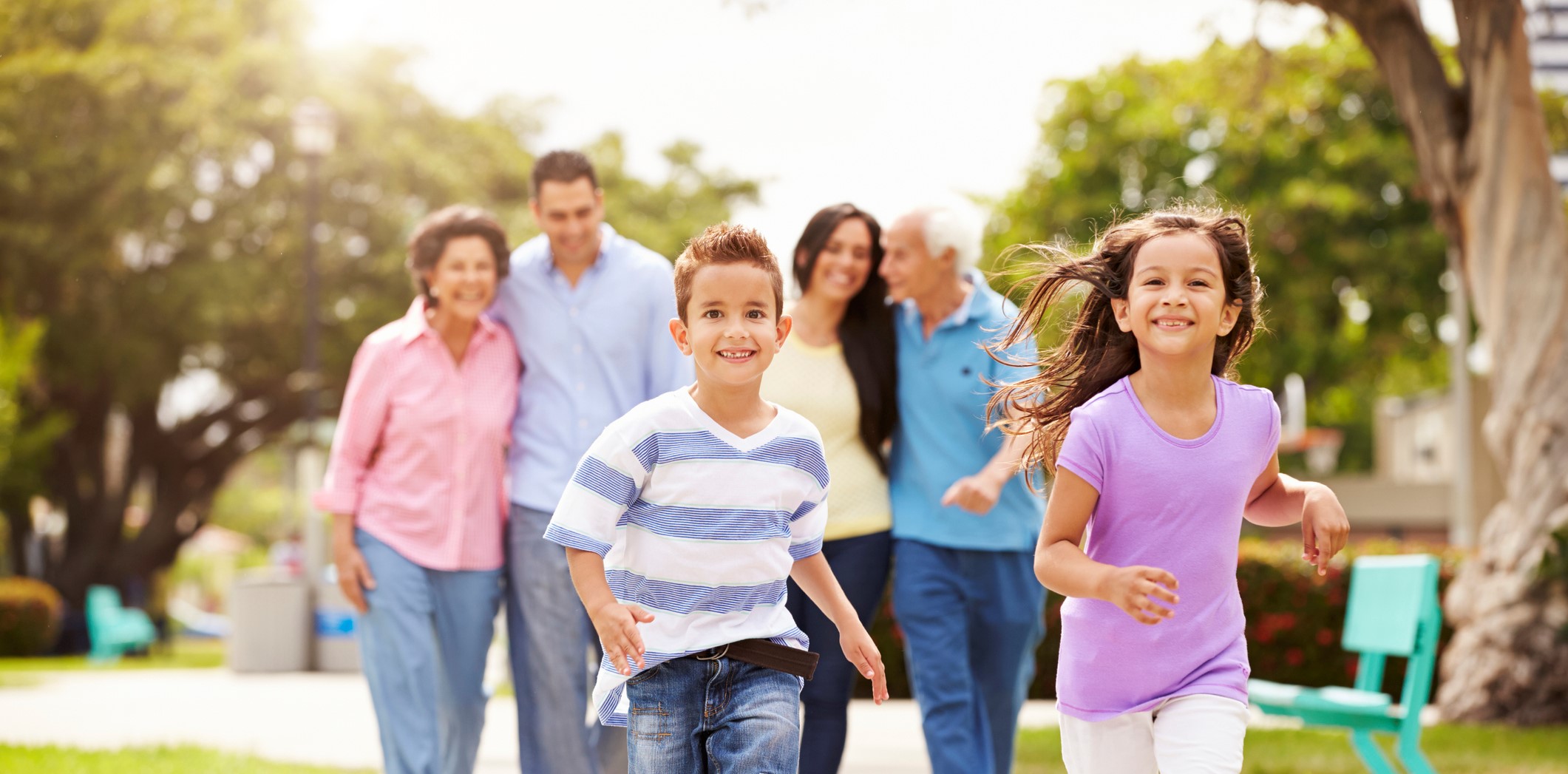 Multigenerational family walking in park together, with children running ahead