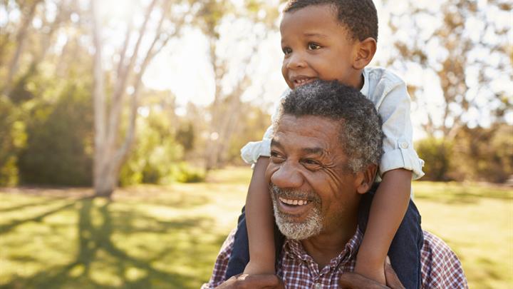 Grandfather carries grandson on shoulders during walk in park