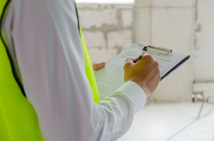 Inspector in reflective green safety vest inspecting construction site, while holding clipboard