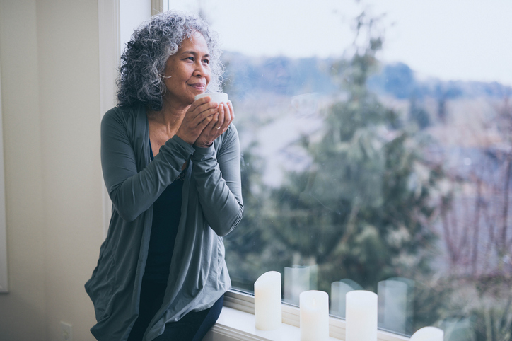 Woman sitting on window sill, looking out contemplatively while holding a cup of tea