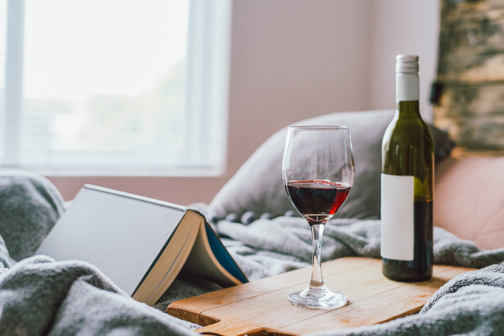 Glass of red wine and a book on the bed at home