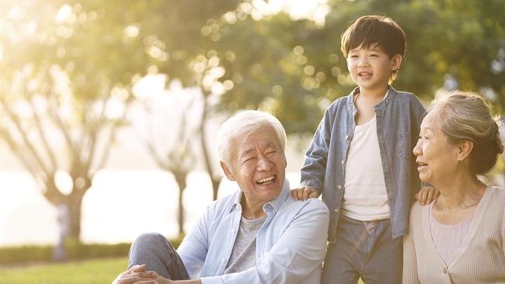 Grandson, grandfather and grandmother sitting, chatting on grass outdoors in park at dusk