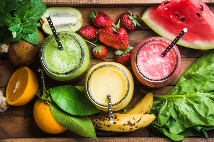 Freshly blended fruit smoothies of various colors and tastes in glass jars in rustic wooden tray