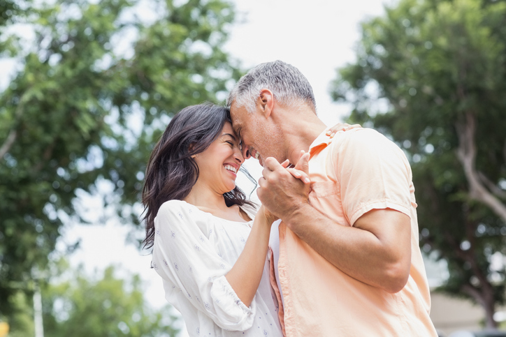 Happy couple dancing against trees in city