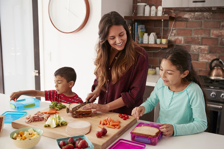 Children helping mother make school lunches in kitchen at home