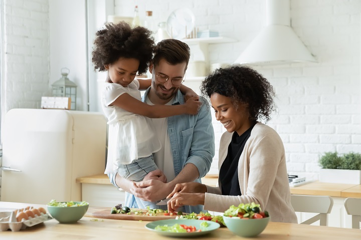 Multiracial family with small girl child preparing a healthy salad in kitchen together