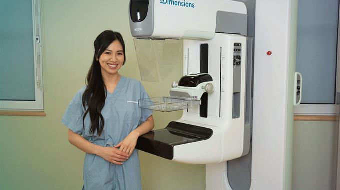 MRT stands next to a mammogram machine and smiles 