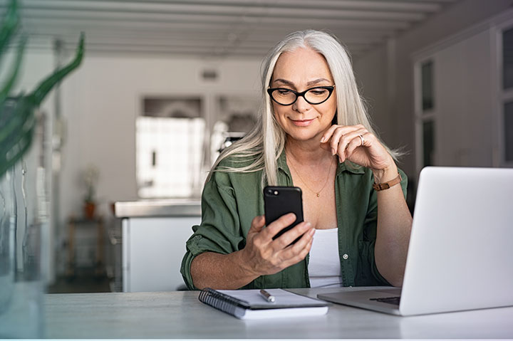 Woman looking at phone with computer in front of her