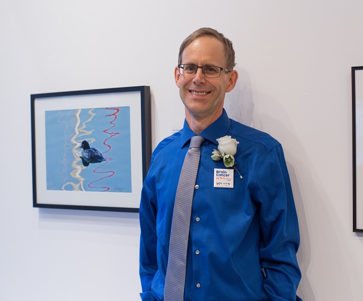 Smiling man stands by photo of duck and reflected lines at art gallery