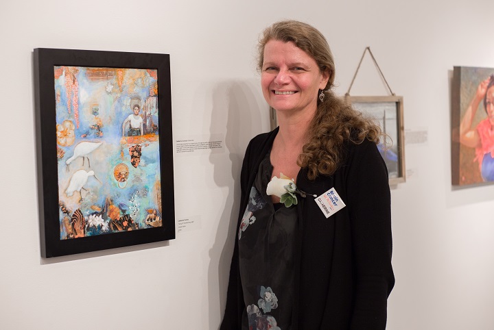 Smiling woman poses in front of painting at art gallery