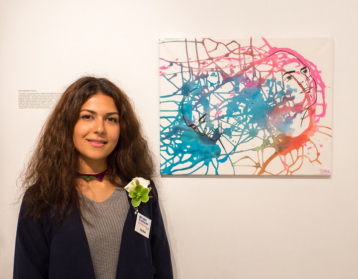 Woman poses in front of painting of two heads joined by paint splatters