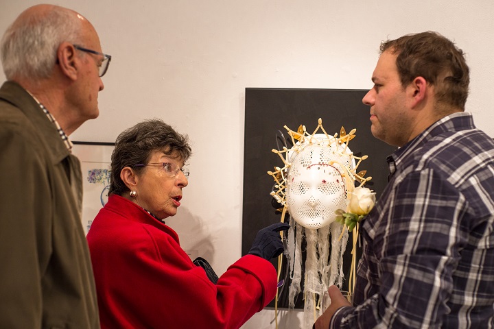 Woman points questioningly at sculpture of head at art gallery, while in conversation with two men