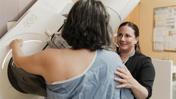 Middle aged woman standing in front of mammogram machine being positioned by a technologist 