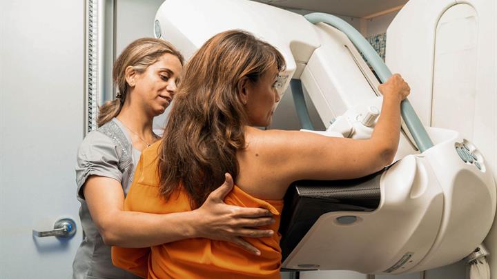 Middle aged woman standing in front of mammogram machine being positioned by a technologist 