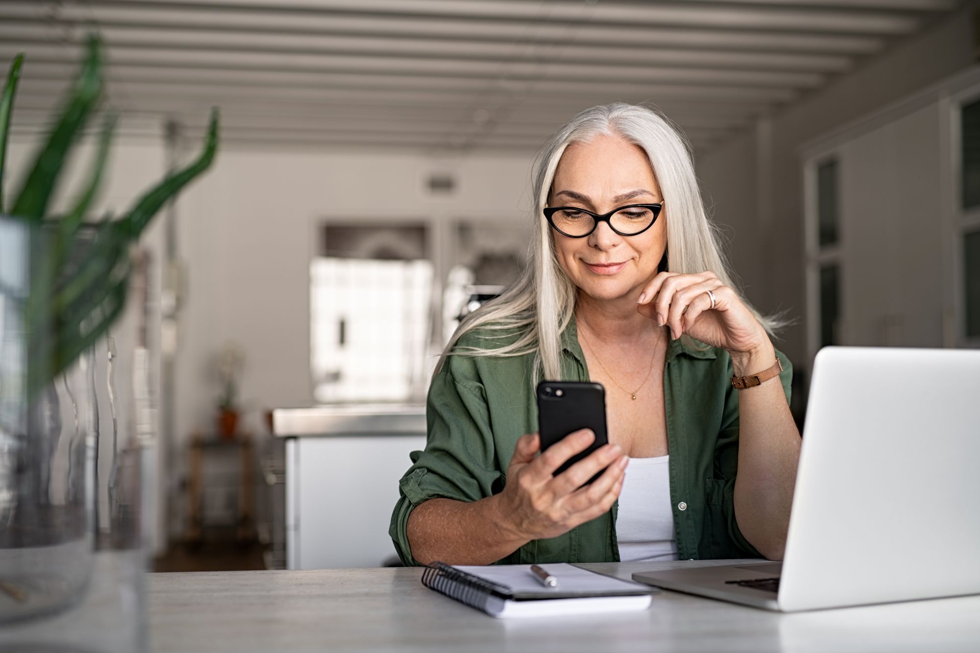 Woman looking at phone with computer in front of her