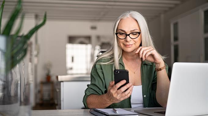 Woman looking at phone with computer in front of her