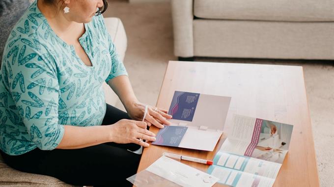 A woman sits on a couch with a cervix self-screening kit laid out in front of her
