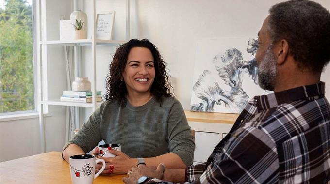 Two people sitting at a kitchen table drinking coffee 
