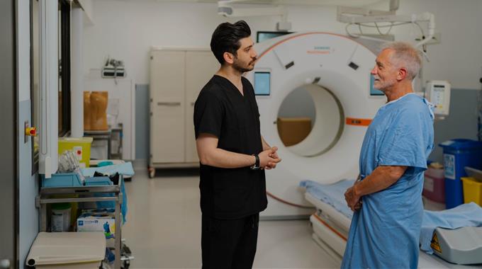 A Technologist talks to a patient in front of a CT scanner 